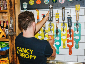 Person in a bar pouring big drop alcohol-free beer from a tap with colorful beer taps on the wall.