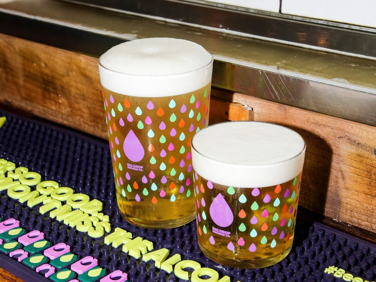 Two alcohol-free beer glasses with colorful drop pattern on a bar mat.
