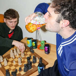 Two people playing chess with a person drinking Big Drop Alcohol-Free Beer from a Branded Pint Glass