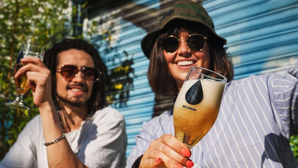 Two people enjoying Big Drop Alcohol-Free beer outdoors in the sunshine.