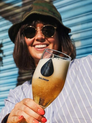 Person holding a Big Drop Alcohol-Free glass of beer outside in the sunshine