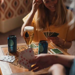 Two people playing cards and enjoying Big Drop Alcohol-Free Pale Ale Cans