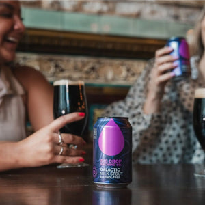 Two people enjoying a glass of Big Drop Galactic Alcohol-Free Milk Stout at a bar.